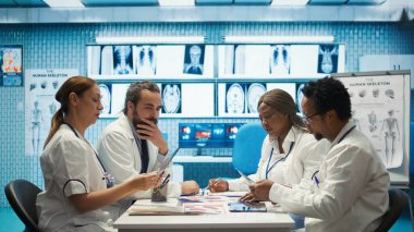 Tedavi protokolleri ve iyileştirmeleri tartışan bir toplantıda sağlık uzmanları. Doktorlar ve hemşireler tıbbi hizmetlerin kalitesini arttırmak için özel bir klinikte teşhis sonuçlarını değerlendiriyorlar. Kamera B.