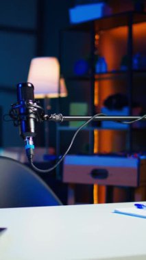 Online şov için video kaydetmek için kullanılan podcast mikrofonunun dikey görüntüsü. Boş oturma odasında neon ışıklı podcast mikrofonunun görüntüsünü yakınlaştır ve kaydet.