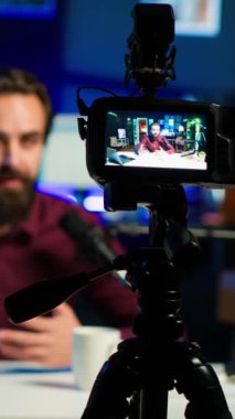 Bulanık arka plandaki adam tarafından kullanılan profesyonel kamera üzerine dikey video odak noktası Neon lit Stüdyoları 'nda internet şovu sunuyor. Vlogger 'ın yayın sırasında kullandığı yüksek teknoloji ekipmanlarını kapat