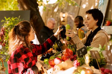 Market alışverişi yapan genç bir kadın, yerel bir satıcıyla sağlıklı ürünler için konuşuyor. Tüketiciye taze organik meyve ve sebze seçiminde yardımcı olan dişi çiftçi.