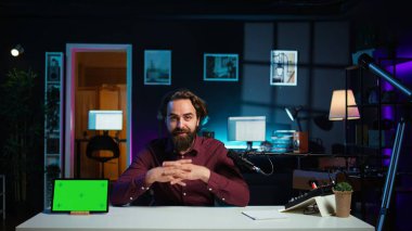 Teknoloji uzmanı, ilgilenen izleyicilere maket tableti sunuyor. Profesyonel mikrofonla çekim yapıyor. Yeşil ekran dijital cihazını inceleyen adam, özel ekipmanlarla kayıt yapıyor, kamera B