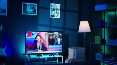 TV ekranında haber yayını ve kayıt cihazları boş ev stüdyosunun içinde görülüyor. Modern apartmanda gece vakti RGB ışıklarıyla aydınlatılan akım ekipmanlarının çekimini yap.
