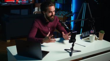 Medya yıldızı stüdyoda tripod dengeleyicisine bağlı akıllı telefondan izleyicilerle konuşuyor. Adam sosyal medya ve kamera B için oturma odasında video kaydetmek için cep telefonu kullanıyor.