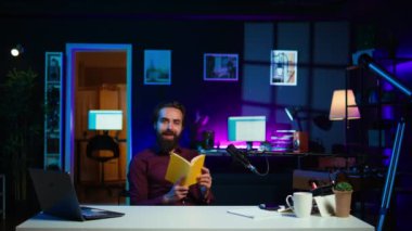 Stüdyodaki gülümseyen nüfuzlu yayınevinin yeni çıkan ciltli kitabını eleştiriyor. Yazardan okuyucuya yeni bir roman sunan mutlu akademisyen edebiyat videosu denemesi çekiyor