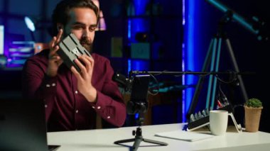 Teknoloji gurusu V mount bataryasını sunuyor, cep telefonunu tripoda ve profesyonel mikrofonda kullanarak teknoloji incelemesi yapıyor. Kafkasyalı vlogger aygıt özelliklerini yüklüyor, telefonla kayıt, kamera A