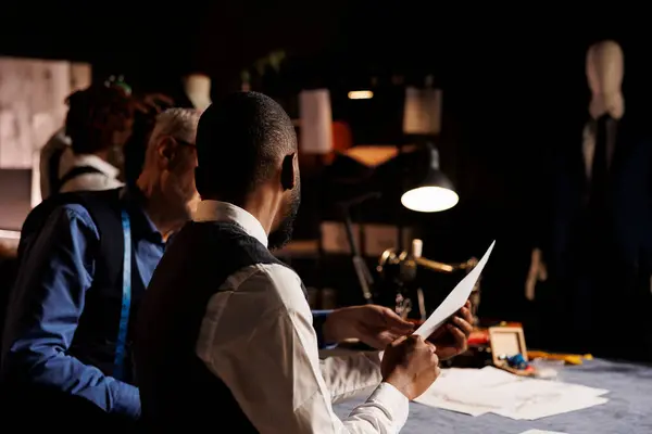 stock image African american client discussing over clothing sketches with skilled craftsman, asking for customization alterations to be done. Suitmaker helping gentleman with bespoke attire in atelier studio