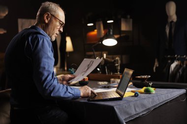 Atölye atölyesinde kişiselleştirme komisyonuna başlamadan önce müşteri randevu listesini kontrol eden deneyimli yaşlı bir terzi. Giysi tasarımı çizimi üzerine çalışan bir terzi.