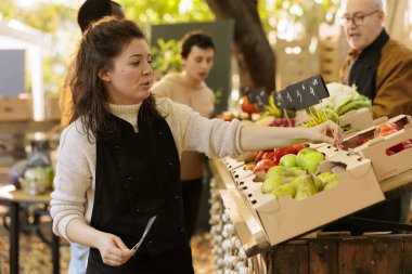 Müşteri organik biyolojik ürün satın alırken, kadın tedarikçi sağlıklı gıda ürünlerine fiyat etiketi koyar. Genç bir tüccar müşterilerine taze, renkli sebze ve meyve satmaya hazırlanıyor..