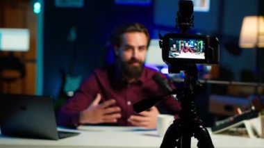 Bulanık arka plandaki adam tarafından kullanılan profesyonel kameraya odaklanın. Neon lit stüdyosunda internet şovu sunuyor. Vlogger 'ın yayın sırasında kullandığı yüksek teknoloji ekipmanlarını kapatın, kamera A