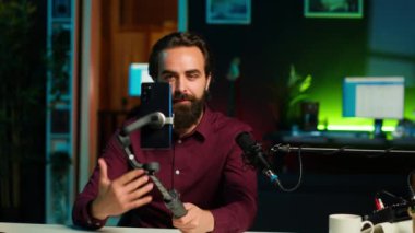 Selfie çubuğunda akıllı telefon kullanarak video çeken, çılgın hareketler yapan etkileyici bir adam. Stüdyoda telefonla video bloğu çekerken hareketli el hareketleri yapan canlandırıcı, kamera A