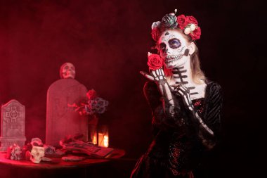 Kırmızı gül tutan bir kadın Dia de los Muerte sırasında ölen akrabalarını onurlandırmak için yerel ayinler yapıyor. Kafatası makyajı yapan kadın, merhumun onuruna Ölüler Günü, Meksika etkinliğine katılıyor.