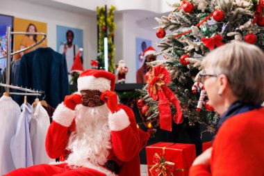 Noel Baba adam alışveriş merkezinde Noel ağacının yanında bayram kutusunu sunarak perakende mağazasında kadınlara hediyeler veriyor. Müşteri, ücretsiz, mevsimlik satışlar için hediye aldıktan sonra heyecanlanıyor.