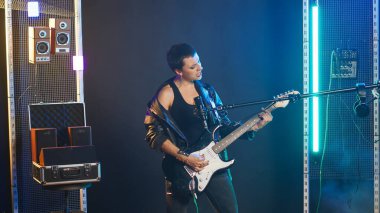 Kadın sanatçı, karanlık bir stüdyoda elektro gitarıyla sahneyi sallıyor, kendine güvenen bir tavır ve asi bir moda sergiliyor. Rock yıldızı heavy metal bir parça çalıyor, alternatif müzik. Kamera B.