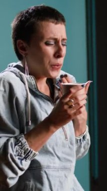 Dikey video kadın model bir fincan kahve içiyor ve stüdyoda dilini yakıyor, sıcak kafein içeceğiyle kendine zarar veriyor. Günlük giysiler içinde şık bir kadın serinletici bir şeyler içiyor. Kamera A.