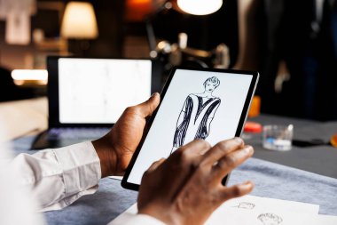 Tasarımcı kadın tarafından yaptırılan zarif elbise tabletine çizilmiş taslak tasarımlarını titizlikle analiz ediyor. Terzi, yaklaşan el yapımı özel elbisenin son detaylarını kontrol ediyor.