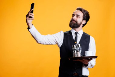 Telefonla fotoğraf çeken, restoran sektöründe çalışan, stüdyoda çatal bıçak tepsisiyle gülümseyen biri. Profesyonel uşak molalarda fotoğraf ve selfie çeker, akıllı telefonu eğlence için kullanır..