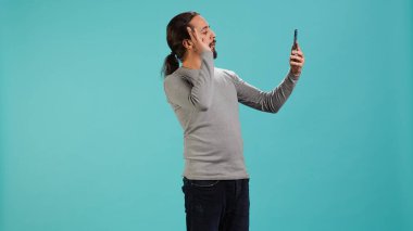 Telekonferans toplantısında arkadaşlarıyla dostça sohbet eden gülümseyen adam akıllı telefon, stüdyo geçmişi kullanıyor. Çevrimiçi video görüşmesi sırasında arkadaşlarla takılırken eğlenen kişi, kamera A