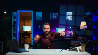 Video çekmek için teknolojik ekipman kullanan oyuncu çılgın hareketler yapıyor. Enerji dolu içerik yaratıcısı sandalyeye atlıyor, profesyonel mikrofonla video bloğu çekerken eğleniyor, kamera B