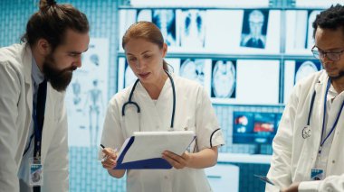 Kabinede test sonuçları ve sağlık kayıtlarını karşılaştıran uzman doktorlar, hastalık önleme konusunda meslektaşlarına danışıyorlar. Muhtelif sağlık görevlileri bir toplantıda profesyonel uzmanlıklarını paylaşıyorlar. Kamera A.