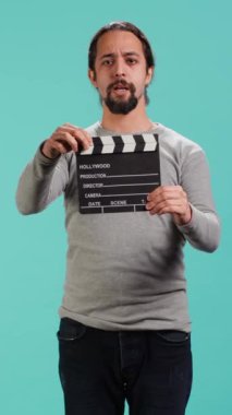 Dikey video yönetmeni oyunculara sahne kaydının, stüdyo arkaplanının sinyalini vermek için klaket kullanıyor. Film yapımcısı sette video yapımcılığı yapıyor. Alkış tahtası, kamera A kullanıyor.