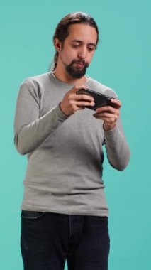 Dikey Video Adam, akıllı telefondan tek kişilik video oyunları oynayarak hobisinden keyif alıyor. Oyuncu telefondaki interaktif oyundan zevk alıyor, eğleniyor, stüdyo arka planında izole edilmiş, kamera A