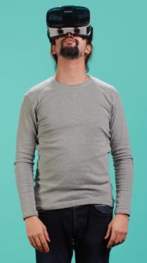 Sanal gerçeklik gözlüğü takıp etrafa bakınan dikey video heyecanlı teknoloji hayranı. Arap adam ileri teknoloji modern VR gözlükleri kullanıyor, dokunaklı hareketler yapıyor, stüdyo arka planı, kamera A