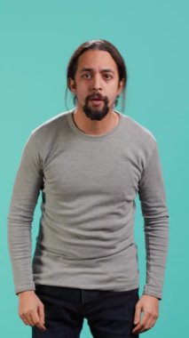 Yüzünü elleriyle örten korkmuş bir adamın dikey video görüntüsü stüdyo arka planında izole bir şekilde duruyor. Korkmuş yüz ifadesi olan, şoka uğrayan, perişan olmuş, korkmuş bir insan.