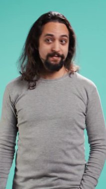 Dikey videoda gülümseyen adam arkadaşlarıyla selamlaşıyor, onları gördüğüne seviniyor, mavi stüdyo arka planında soyutlanmış. Dost canlısı el sallayan kişi, selam veren arkadaşlar, arkadaş canlısı olmak, stüdyo arka planı, kamera B