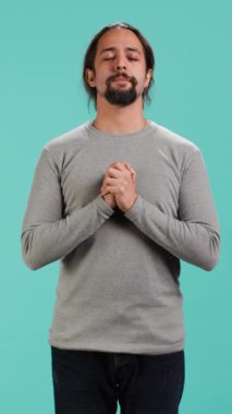 Dikey video rahatlamış adam gökyüzüne bakıyor, gözlerini kapıyor, tanrısından işaret bekliyor. Zen manevi adam el hareketleriyle ibadet ediyor, mucize umuduyla, stüdyo arka planında izole edilmiş, kamera A