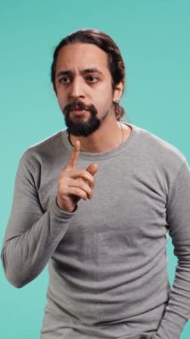 Susma hareketi yapan bir adamın dikey video görüntüsü, sessizlik talep ediyor. Dudaklara parmak basan, sessiz işaret hareketi yapan, gizlilik isteyen, stüdyo arka planında izole edilmiş, kamera B