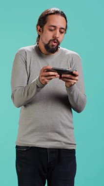 Dikey video odaklı adam cep telefonunda yoğun video oyunu oynar, dokunmatik ekranda spam saldırı tuşları. Oyun yarışmasına katılan oyuncu, stüdyo arka planında izole edilmiş, kamera A