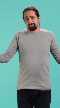 Dikey videocu omuz silkiyor, belirsizlik ve çaresizliği ifade ediyor, yüz ifadesi sorunlu. Arkadaşına yardım edemeyen, güçsüz hisseden, stüdyo geçmişi olan biri.