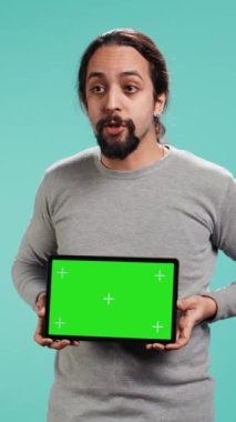 Yeşil ekran tableti sunan dikey video etkileyicisi, stüdyo arka planında izole edilmiş. Arap kişi, reklam markaları, stüdyo arkaplanı, kamera B için kullanılan boş krom anahtar cihazını elinde tutuyor.