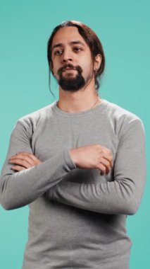 Gülümseyen, mutlu görünen, mavi stüdyo arka planında izole edilmiş neşeli bir Arap 'ın dikey videosu. Mutlu dışavurumcu kişi şık giyinmiş sırıtıyor, tatmin olmuş hissediyor, kamera B