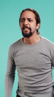 Öfkeli bir adamın öfkeli hissettiği dikey video portresi, arkadaşına bağırması, bastırılmış duygularını açığa vurması, stüdyo arkaplanı. Öfke dolu öfkeli insan, mavi stüdyo arka planında izole edilmiş arkadaşına bağırıyor.