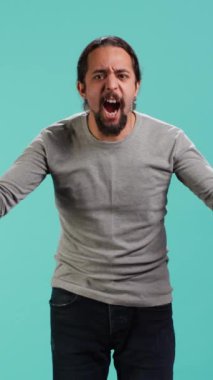 Öfkeli bir adamın öfkeli hissettiği dikey video portresi, arkadaşına bağırması, bastırılmış duygularını açığa vurması, stüdyo arkaplanı. Öfke dolu öfkeli insan, mavi stüdyo arka planında izole edilmiş arkadaşına bağırıyor.