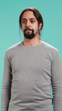 Mavi stüdyo arka planında izole bir şekilde duran ciddi bir Arap 'ın dikey videosu. Odaklanmış ifadesi olan kendine güvenen, kararlılık ve özgüven öneren kişi, stüdyo arkaplanı