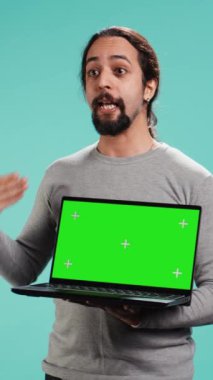 Dikey video teknolojisi içerik yaratıcısı yeşil ekran dizüstü bilgisayar kullanarak pazarlama yapıyor, stüdyo arka planında izole edilmiş. Arap adam elinde boş bir fotokopi defteri tutuyor, inceleme yapıyor, kamera B