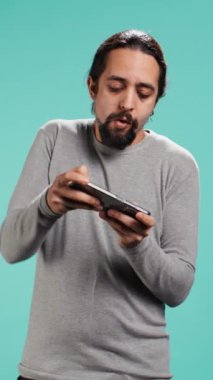 Dikey video odaklı adam cep telefonunda yoğun video oyunu oynar, dokunmatik ekranda spam saldırı tuşları. Oyuncu oyun yarışmasına katılıyor, stüdyo arka planında izole edilmiş, kamera B