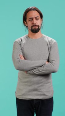 Dikey video Huysuz Adam kollarını kavuşturuyor, olaylardan rahatsız oluyor, stüdyo arka planında soyutlanıyor. Stresli, huysuz, başını sallayan, rahatsız edici haberlerle nutku tutulmuş, kamera A