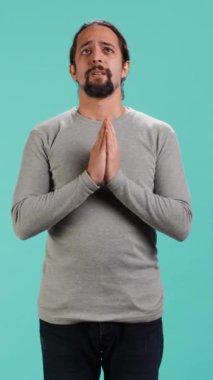 Bir adamın el ele tutuşup, dilek tutarak stüdyo arka planında iyi haberler beklediği dikey video görüntüsü. Sonuçları bekleyen, olumlu sonuç için dua eden kişi