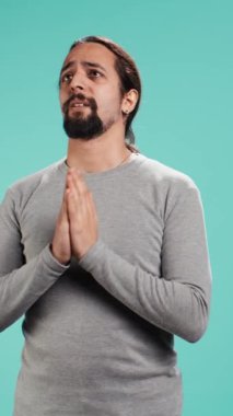 Bir adamın el ele tutuşup, dilek tutarak stüdyo arka planında iyi haberler beklediği dikey video görüntüsü. Sonuçları bekleyen, olumlu sonuç için dua eden kişi