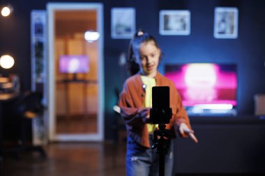 Dans eden, şarkı söyleyen, sosyal medya için video çeken bir kızın kullandığı tripoda odaklan. Bulanık arka plandaki çocuk telefonla kaydedilen profesyonel koreografili aboneleri eğlendiriyor