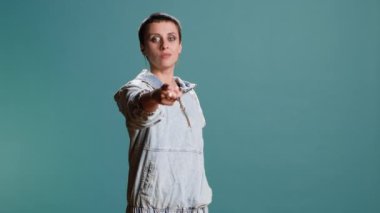 Manyak havalı genç bir kadın işaret parmağını kameraya doğrultuyor. Mavi arka planda birini seçiyor. Sokak tarzı ve şehir kıyafetleri olan modern bağımsız bir kız. Kamera B.