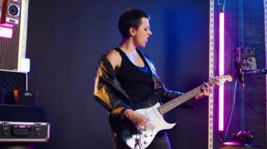 Baş parmaklarını gösteren ve gitar çalan bir kadın, stüdyoda müzik performansı. Kadın rockçı, olumlu bir işaretle onayını veriyor. Kamera A.
