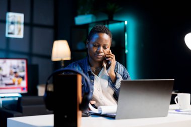 Afrika kökenli Amerikalı serbest çalışan kadın müşteriyle mobil cihazda sohbet ederken ev bilgisayarından faydalanıyor. Zenci kadın uzaktan çalışıyor, belgeleri inceliyor ve telefon görüşmeleri yapıyor..
