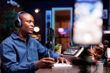 Stüdyodaki Afrikalı Amerikalı etkili canlı yayın kanalı için yüksek teknolojili bir mikrofon kullanıyor. Profesyonel yayın ses donanımı kullanarak podcast yapan bir adam,