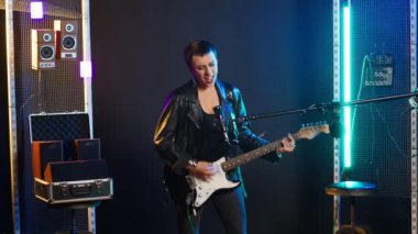 Edgy female performer plays an acoustic guitar in a nightclub, performing with fierce energy and bold fashion. Singer heavy metal artist singing alternative music, wild atmosphere. Camera B.