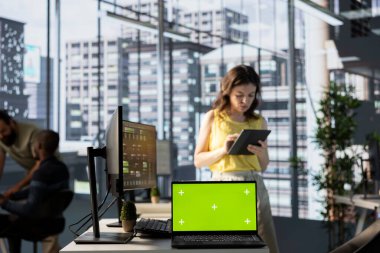 Yöneticinin önündeki yeşil ekran dizüstü bilgisayar yazılım kalite güvencesi veriyor, tabletteki kaynak kodunu kontrol ediyor. Ofiste Chroma anahtar defteri ile çalışan bir kadın cihazdaki kodlamayı denetliyor.