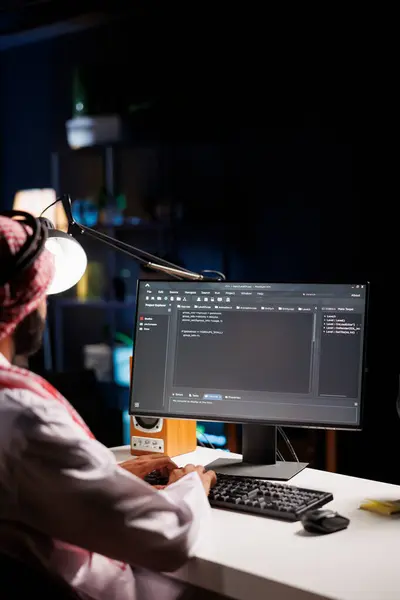 stock image Traditional Middle Eastern developer compiles code on desktop computer, showcasing expertise in programming, algorithms, and software development. Selective focus on pc monitor displaying source code.